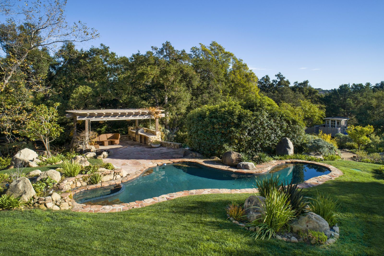 The lush grounds of a Montecito estate, with a free-form pool, cabana, mature trees, and a hint of ocean view